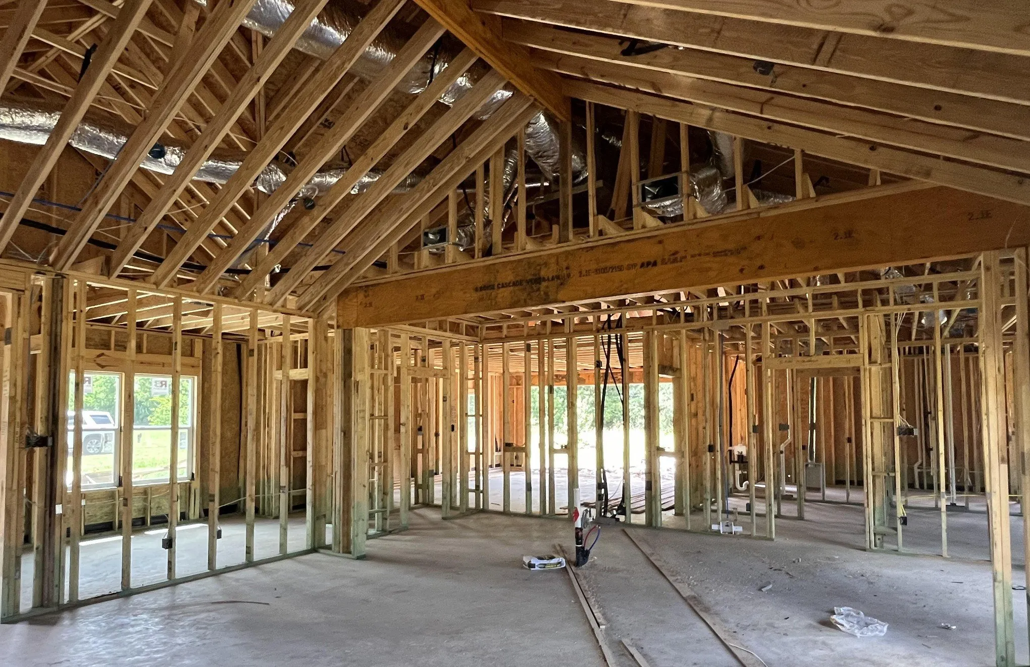 Interior of a home under construction, showing exposed wood wall framing, roof trusses and ductwork
