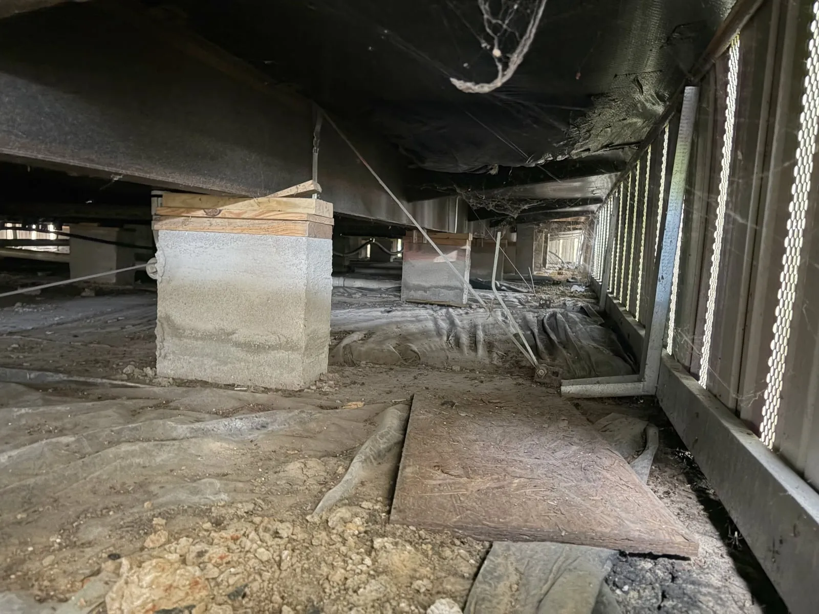 Underside of a manufactured home showing concrete block piers, wood shims and anchor straps supporting the steel chassis frame