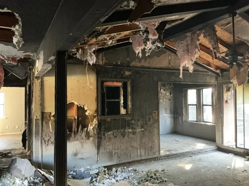 Fire-damaged home interior with charred ceiling joists, burned wall framing and fallen insulation